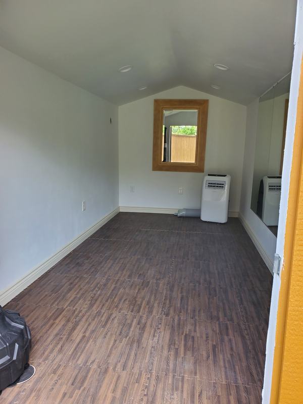 Small finished room with white walls and a vaulted ceiling, a window, wood-look plank flooring and a large wall mirror