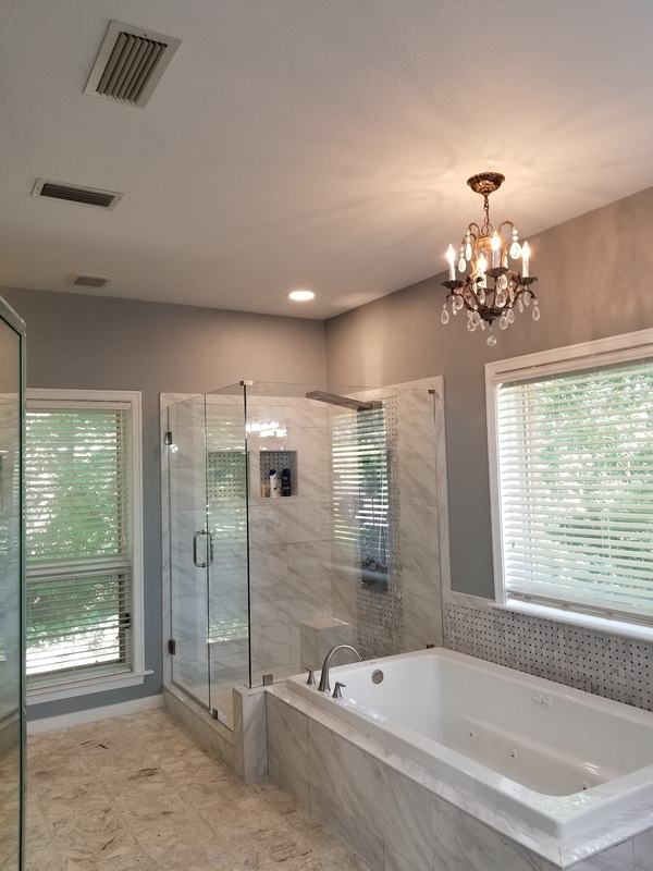 Remodeled bathroom with marble-look tile, a frameless glass shower, a soaking tub and a chandelier