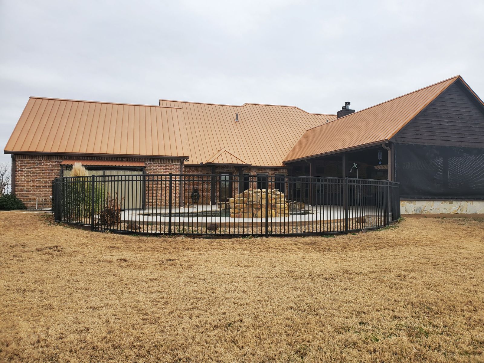 Long single-story brick home with a new copper-colored standing-seam metal roof, a screened porch and a pool fence