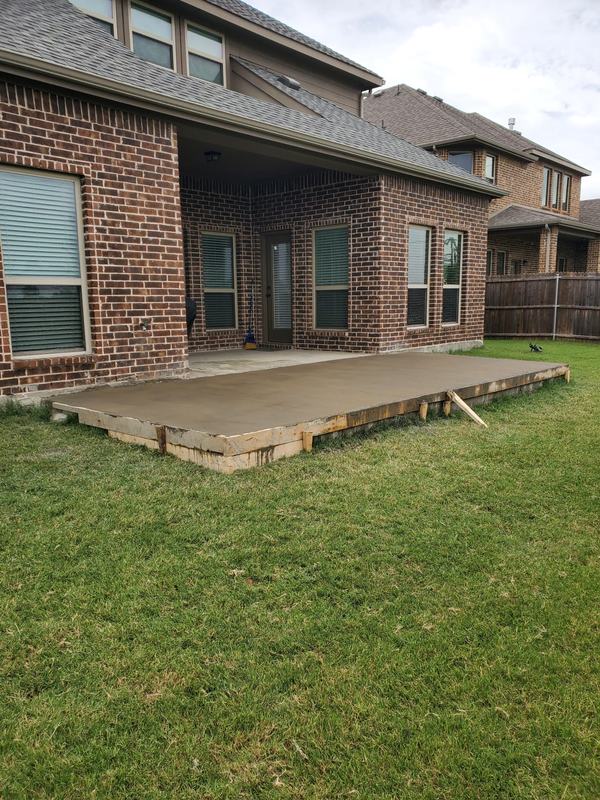 Freshly finished concrete patio slab with edge forms beside the back of a two-story brick home