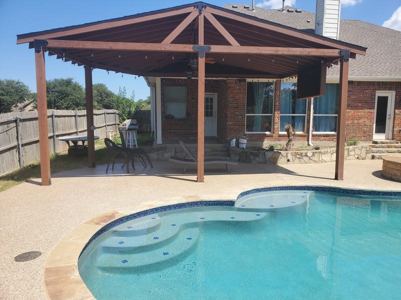 Backyard pool with a blue tile step bench in front of a covered timber patio and a brick home